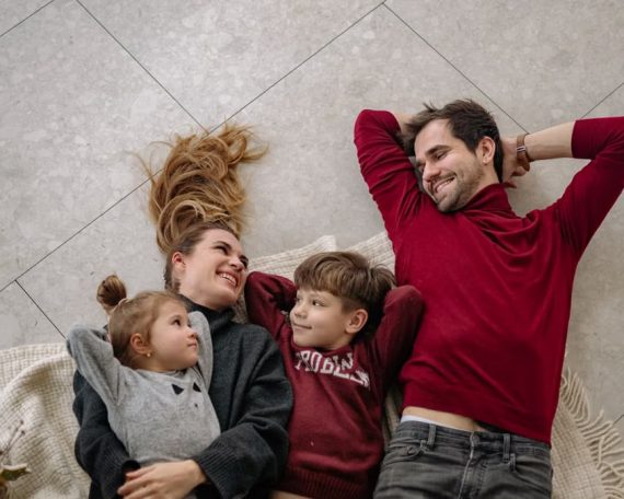 Smiling family of four lying on a blanket, sharing happiness and love indoors.