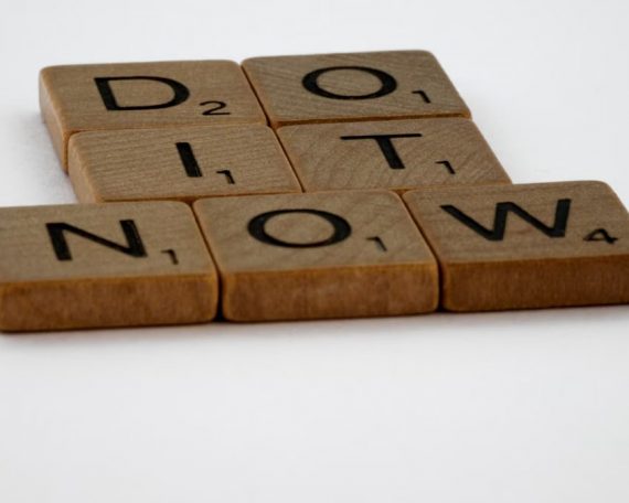 Wooden Scrabble tiles spelling 'Do It Now' on a white background. Motivational concept.
